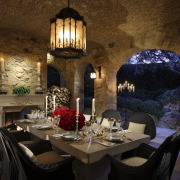 View of outdoor dining area with stone walls. dining room, home, interior design, lighting, restaurant, room, table, brown, black