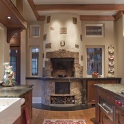 View of kitchen fireplace and red floor rug. cabinetry, ceiling, countertop, cuisine classique, fireplace, floor, flooring, hardwood, hearth, home, interior design, kitchen, living room, room, wall, wood flooring, brown