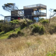 View of multilevel home on tussocky slope. - architecture, building, cottage, grass, home, house, land lot, property, real estate, sky, brown, white