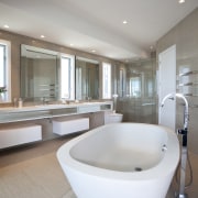 Bathroom with large white tub and beige walls. architecture, bathroom, bathtub, floor, interior design, plumbing fixture, real estate, room, gray