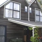 View of brown timber house with sqaure windows. cottage, facade, home, house, property, real estate, roof, siding, window, black, gray