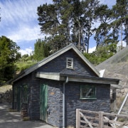 Exterior view of stone building with wooden fence. cottage, farmhouse, home, house, hut, log cabin, property, real estate, shack, shed, sky, tree, wood, gray, teal, black