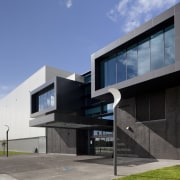 Exterior with dark grey cladding. - Exterior with architecture, building, commercial building, corporate headquarters, elevation, facade, headquarters, home, house, real estate, residential area, teal, gray, black