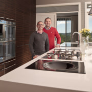 Two men in a kitchen with brown wooden countertop, home appliance, interior design, kitchen, kitchen appliance, white, red