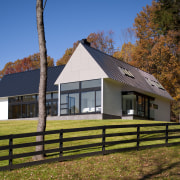 Clapboard siding and a metal roof place this barn, cottage, estate, facade, farmhouse, grass, home, house, property, real estate, rural area, sky, tree, brown