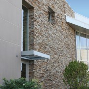 A wall of natural stone has a  rugged architecture, brick, building, cottage, estate, facade, home, house, neighbourhood, property, real estate, residential area, siding, sky, suburb, wall, window, gray