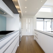 This galley-style kitchen showcases a full suite of ceiling, countertop, daylighting, floor, home, house, interior design, kitchen, property, real estate, room, white