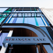 Close-up of STRANGES LANE sign  Above:Standing proud architecture, building, commercial building, daylighting, facade, line, metropolitan area, roof, sky, structure, urban area, black, white