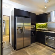 The kitchen in this renovated 1970s apartment features cabinetry, countertop, home appliance, interior design, kitchen, major appliance, real estate, refrigerator, black