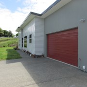 The exterior of this four-bedroom family residence designed asphalt, door, facade, garage, garage door, home, house, property, real estate, residential area, siding, window, gray