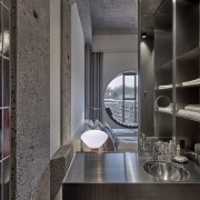 Exposed concrete surfaces contribute to the hotel's industrial-chic architecture, building, cabinetry, cupboard, furniture, house, interior design, loft, property, room, shelf, shelving, tile, black, gray