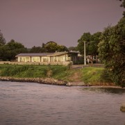 Following an "L" shape plan, the plan is bank, bayou, body of water, building, canal, channel, home, house, lake, landscape, natural landscape, reflection, river, rural area, sky, tree, water, water resources, watercourse, waterway, gray, brown