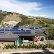 An array of solar panels powers this green architecture, building, estate, highland, hill station, home, house, mountain, mountain range, mountainous landforms, property, real estate, residential area, roof, sky, slope, solar energy, solar panel, solar power, sunlight, technology, brown