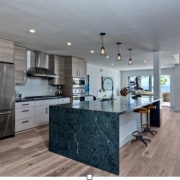 A waterfall island provides space for food prep cabinetry, countertop, cuisine classique, floor, flooring, hardwood, interior design, kitchen, real estate, room, wood flooring, gray