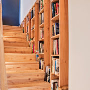 A bookshelf integrated into the stairway wall - bookcase, floor, flooring, furniture, hardwood, home, shelf, shelving, stairs, wood, orange, white