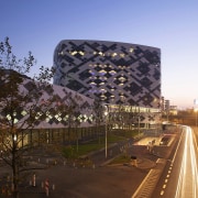 The airport hotel sits adjacent to a main architecture, building, city, corporate headquarters, evening, headquarters, landmark, metropolis, metropolitan area, mixed use, night, residential area, sky, skyscraper, structure, tourist attraction, tower block, tree, urban area, brown