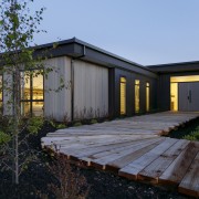 ​​​​​​​A timber boardwalk leads to a solid front architecture, backyard, building, cottage, estate, facade, home, house, landscape, property, real estate, residential area, roof, shed, siding, tree, window, wood, yard, black