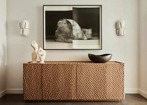 In the foyer a gouged wood credenza is 