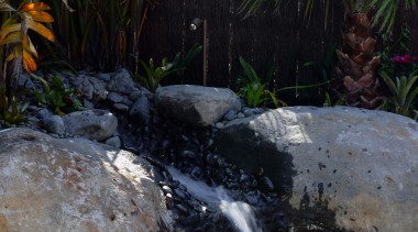 Closeup of waterfall feature going into swimming pool. arecales, body of water, landscape, landscaping, palm tree, plant, pond, swimming pool, tropics, vegetation, water, water feature, water resources, watercourse, waterfall, black