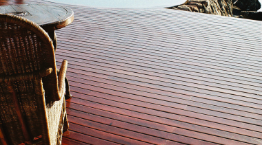 A view of some wooden decking. - A calm, horizon, reflection, sea, shore, sky, water, wood, white, red