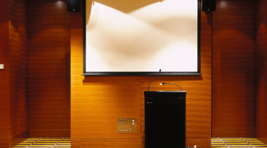 Function room with black podium, white screen and display device, flooring, furniture, interior design, projection screen, room, brown