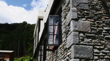 View of exterior of home clad in stone. building, cottage, facade, house, sky, stone wall, wall, window, black, gray