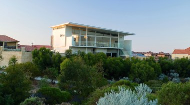 Exterior view of this beach house nestled amongst architecture, city, estate, home, house, landscape, neighbourhood, plant, property, real estate, residential area, sky, suburb, tree, villa, teal