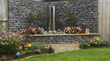 A view of a garden wall made out backyard, flower, garden, home, landscape, landscaping, outdoor structure, plant, stone wall, walkway, wall, yard, gray