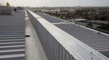 The building's roof was supplied and installed by asphalt, bridge, daylighting, fixed link, guard rail, infrastructure, line, metropolitan area, road, road surface, roof, sky, structure, walkway, gray