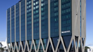 The Novotel Auckland Airport hotel's intricate concrete structure architecture, building, commercial building, condominium, corporate headquarters, daytime, facade, headquarters, landmark, metropolis, metropolitan area, sky, structure, tower block, urban area, blue, black