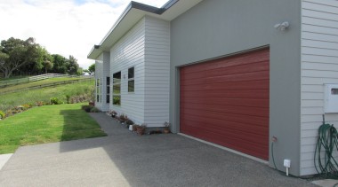 The exterior of this four-bedroom family residence designed asphalt, door, facade, garage, garage door, home, house, property, real estate, residential area, siding, window, gray