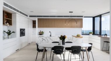 A long marble-clad kitchen island is the central architecture, bar stool, cabinetry, chairs, countertop, dining room, floor, flooring, furniture, home, house, interior design, kitchen, room, table, gray, white, chopping board