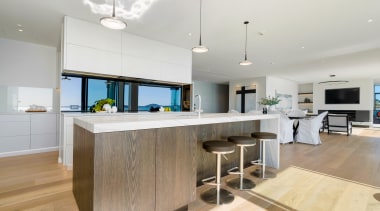 The mirrored splashback behind the cooktop reflects the architecture, building, cabinetry, ceiling, countertop, design, dining room, floor, flooring, furniture, hardwood, home, house, interior design, kitchen, mirror splashback,  mirror backsplash, wood flooring, property, real estate, room, table, wood, wood flooring, gray, white