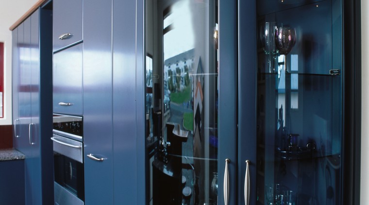 Kitchen with tall blue coloured cabinetry, wall oven cabinetry, display case, glass, black