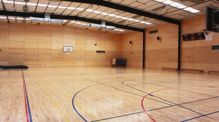 View of large school gym with timber flooring. basketball court, ceiling, floor, flooring, hardwood, indoor games and sports, leisure centre, net, sport venue, sports, structure, wood, wood flooring, orange