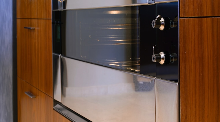 Closeup view of stainless steel oven set into cabinetry, countertop, furniture, home appliance, kitchen, major appliance, gray, brown