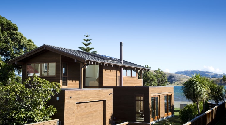 The sides and street facade of this contemporary cottage, estate, facade, home, house, outdoor structure, plant, property, real estate, residential area, roof, sky, tree, villa, teal