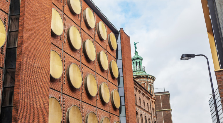 Adorning the shell of the building are over architecture, brick, brickwork, building, city, downtown, facade, iron, metropolitan area, neighbourhood, signage, sky, street, town, urban area, wall, white, orange