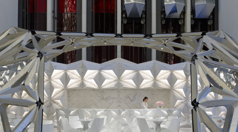 Glass elevators rise behind the faceted reception desk chair, floor, flooring, furniture, table, window, gray, black