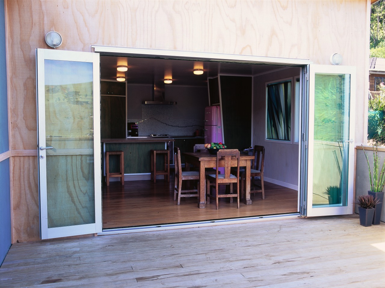 Glass foldback doors open wide providing flow from door, floor, house, outdoor structure, patio, porch, window, white, gray