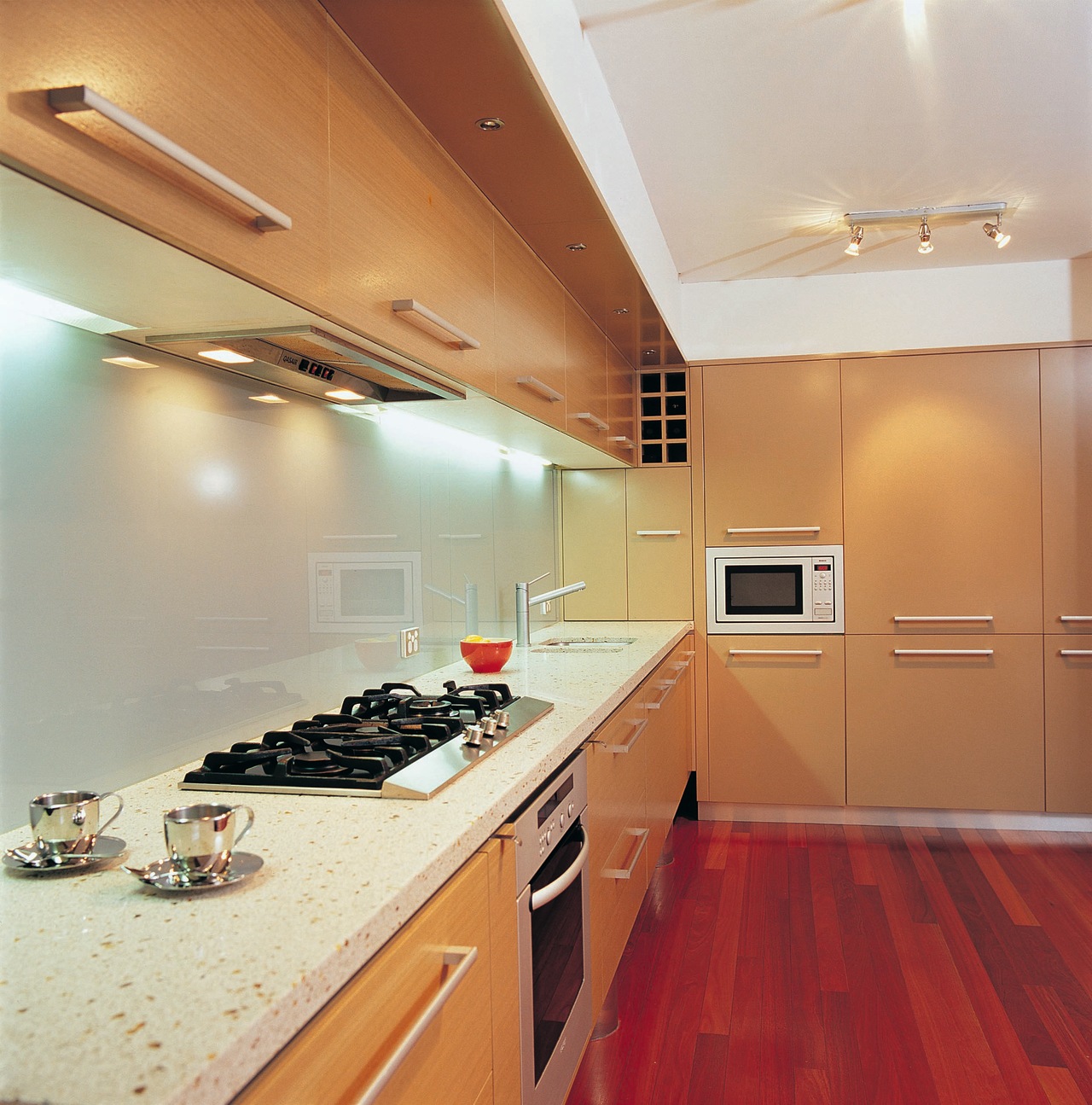 Kitchen with light veneer cabinetry and storage, white cabinetry, ceiling, countertop, floor, flooring, interior design, kitchen, room, under cabinet lighting, orange, gray