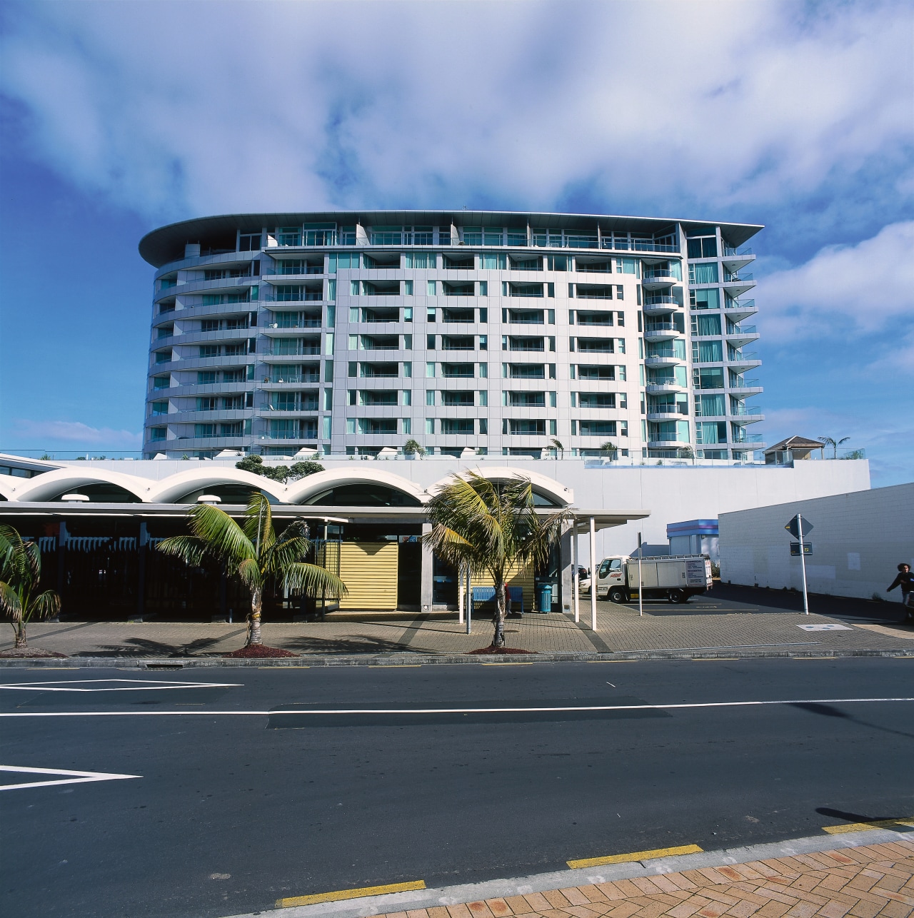 Exterior view of multi-storey apartment building from street. apartment, architecture, building, commercial building, condominium, corporate headquarters, daytime, facade, headquarters, hotel, metropolitan area, mixed use, real estate, residential area, sky, teal, black