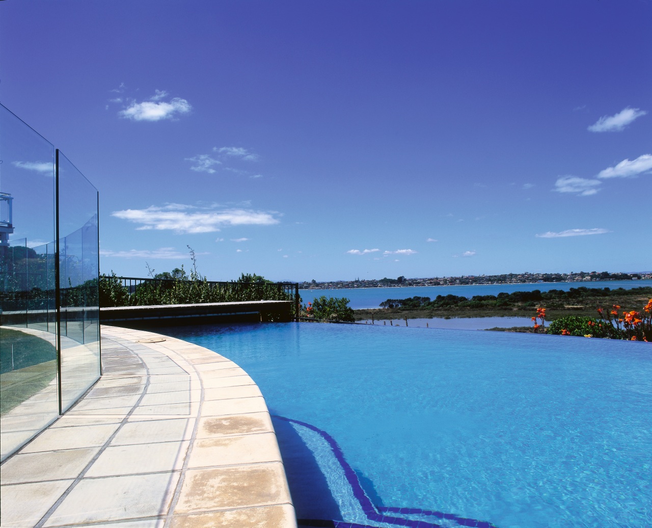 Large blue outdoor pool with natural coloured paving, cloud, daytime, horizon, real estate, reflection, sea, sky, swimming pool, tree, water, waterway, blue