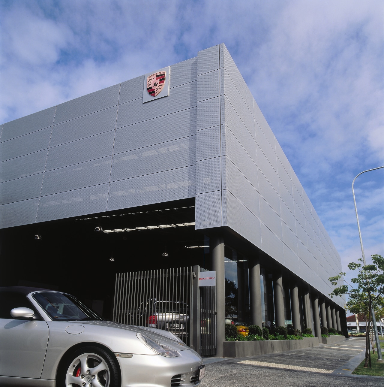 view of the porsche showroom building with heavy architecture, automotive design, building, car, corporate headquarters, facade, luxury vehicle, motor vehicle, parking, sky, vehicle, teal