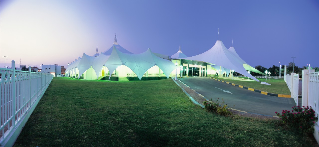 Exterior view of building featuring large canopy structure architecture, grass, landmark, plant, sky, structure, tree, blue