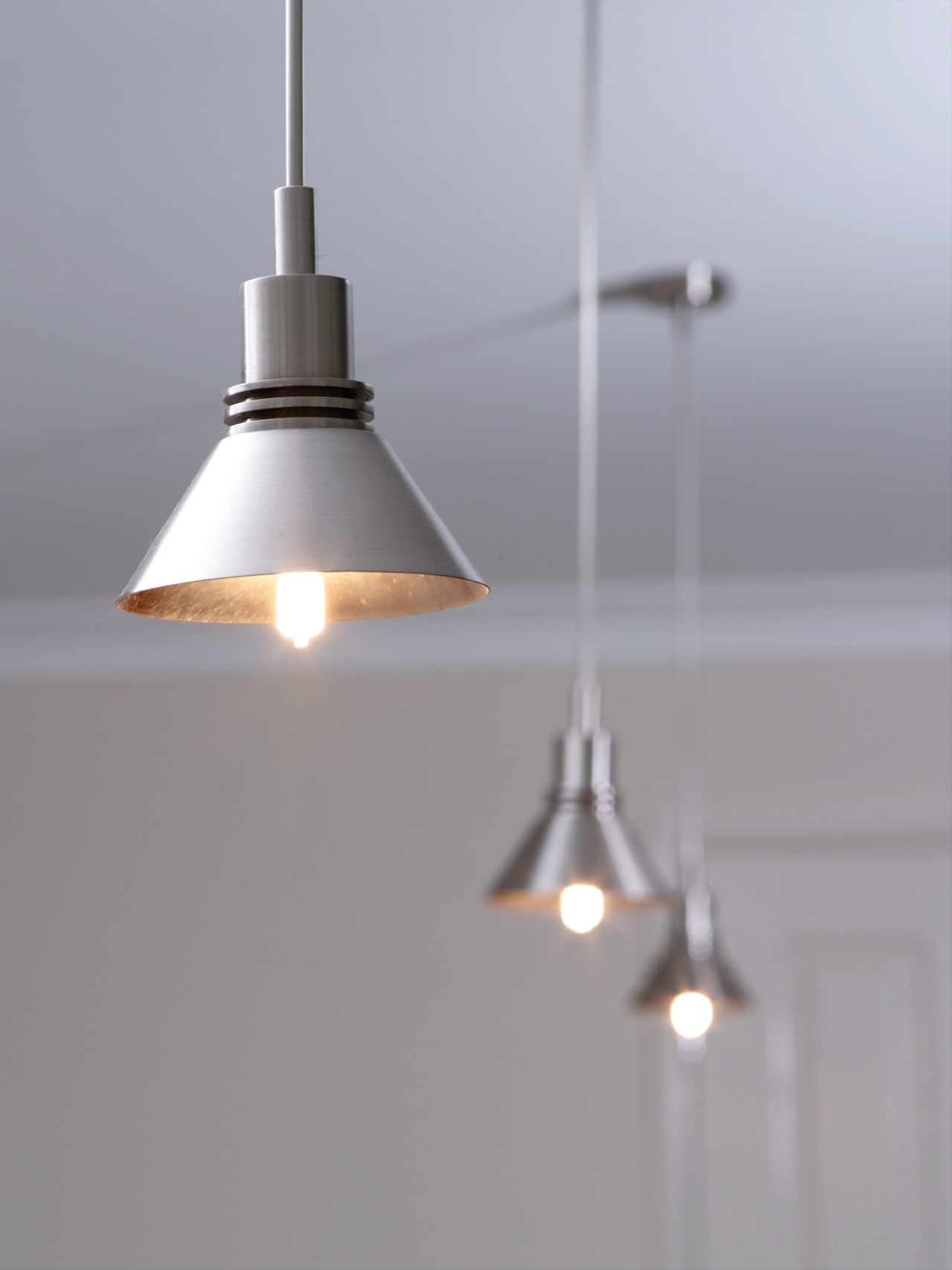 Row of brushed chrome pendant lights. ceiling fixture, lamp, light, light fixture, lighting, lighting accessory, product design, gray