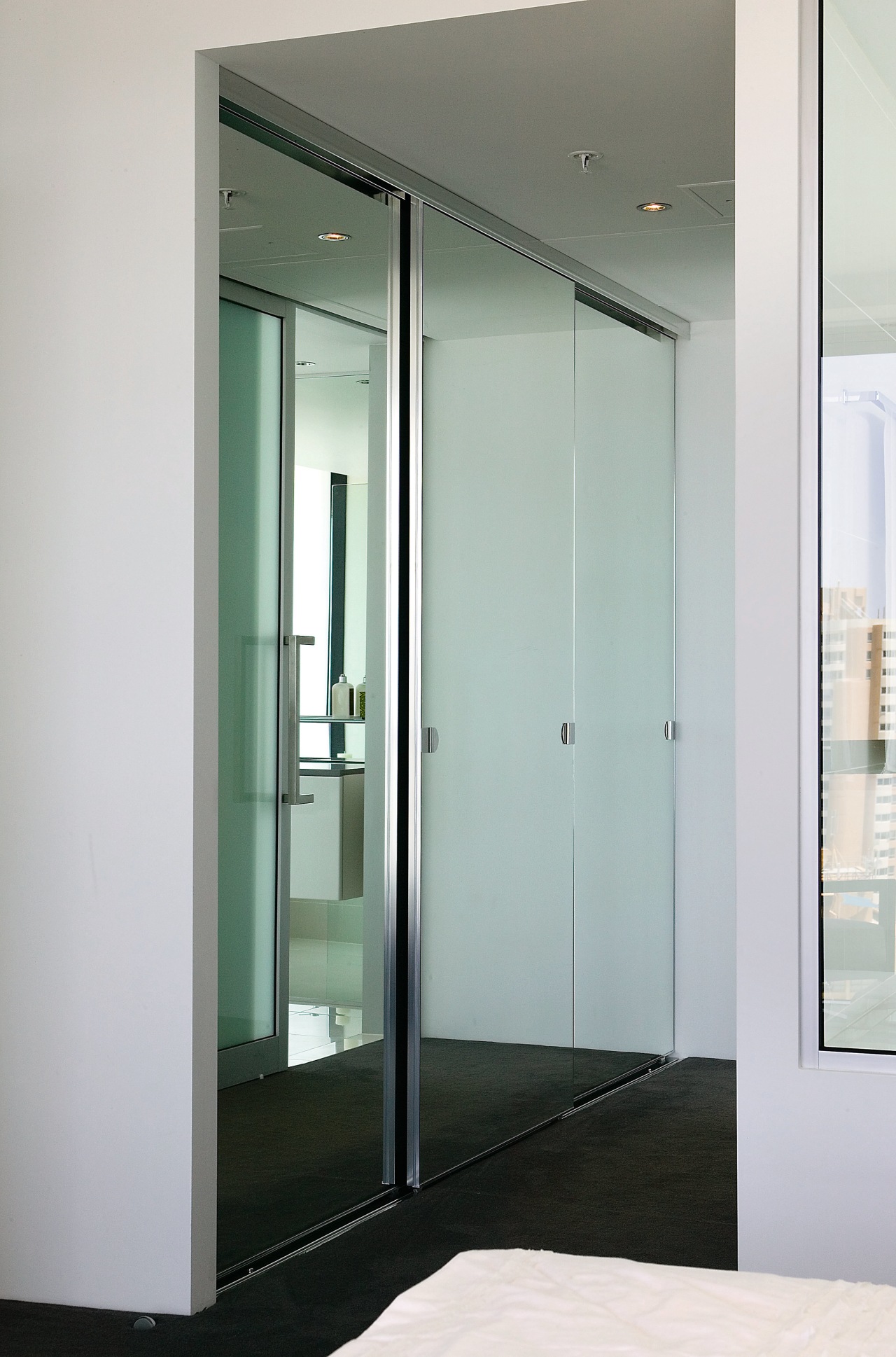 A view of the bedrrom featuring frameless mirrored door, glass, gray