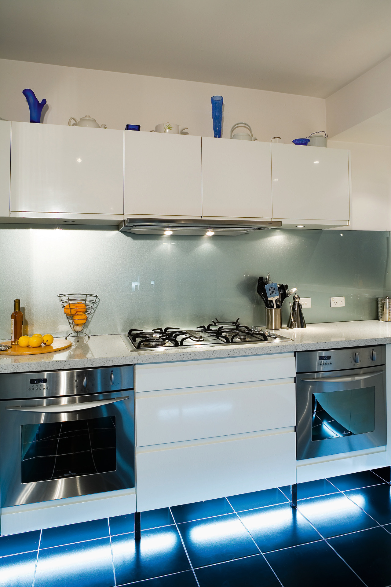 A view of this kitchen featuring tiled flooring, countertop, glass, interior design, kitchen, major appliance, room, under cabinet lighting, gray