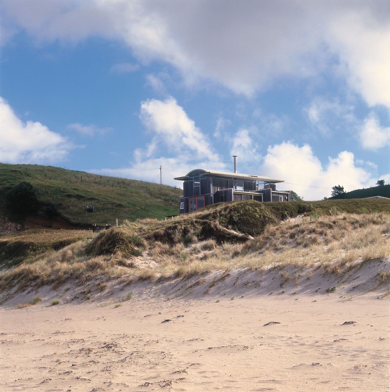 An exterior view of this coastal property on beach, cloud, coast, ecoregion, hill, sand, sea, sky, terrain, orange, gray