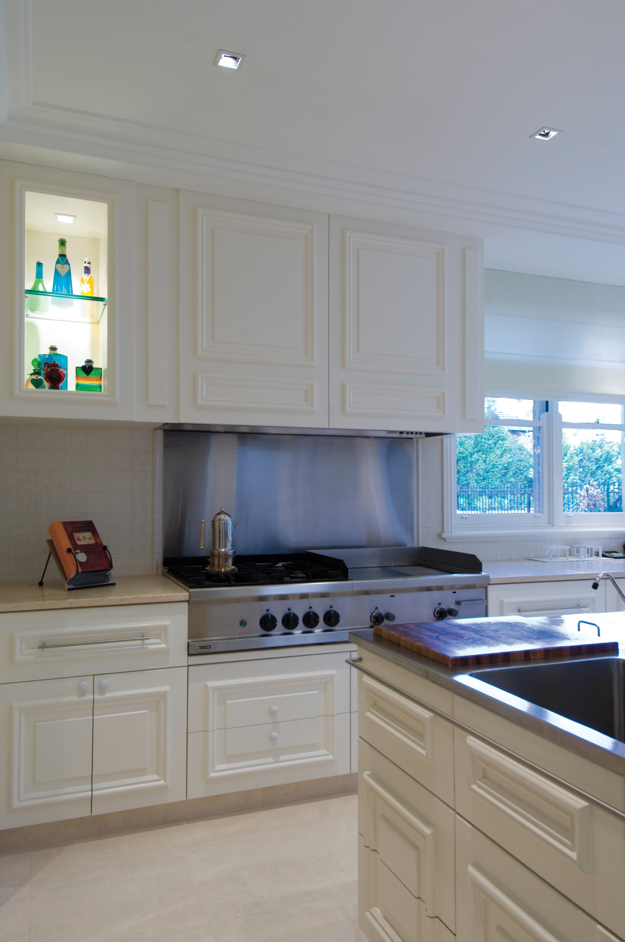 A view of the kitchen featuring cream cabinetry, cabinetry, countertop, cuisine classique, floor, flooring, home, home appliance, interior design, kitchen, room, window, gray